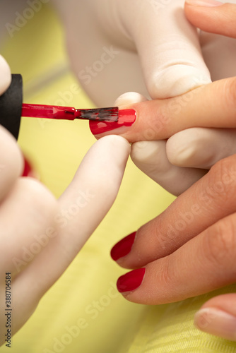 Fototapeta Woman applying red nail polish at manicure salon, close up.