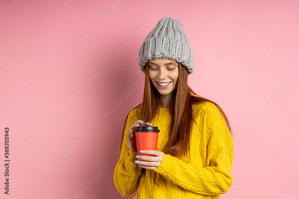 Shot of happy caucasian woman with long red hair holding takeaway coffee, enjoying break, smiling with white teeth looking at camera posing against pink background with copy space for advertising. Shot of happy caucasian woman with long red hair holding takeaway coffee, enjoying break, smiling with white teeth looking at camera posing against pink background with copy space for advertising.