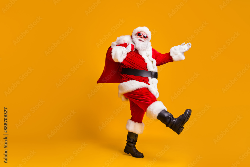 Full body profile side photo of santa claus with big belly beard carry x-mas present gift sack go wear headwear cap sunglass isolated over bright shine color background Full body profile side photo of santa claus with big belly beard carry x-mas present gift sack go wear headwear cap sunglass isolated over bright shine color background