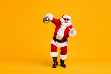 Full body photo crazy santa claus with grey beard hold disco ball show horns symbol dance x-mas christmas party wear sunglass headwear cap isolated bright shine color background