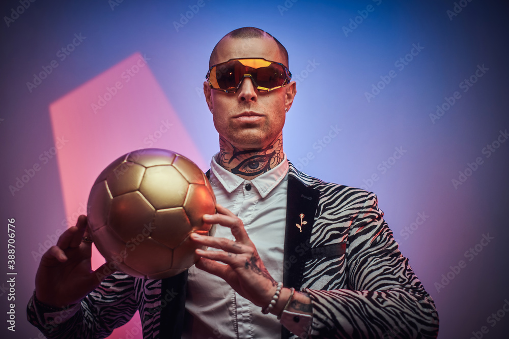 Plakat Styled and futuristic guy with eyewears poses with golden soccer ball in abstract background.
