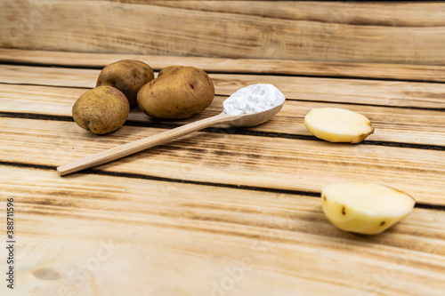 Wooden spoon with starch and a bunch of potatoes on a wooden background.