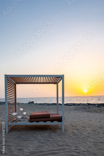 Empty double sun bed on the sandy beach in Dubai  with orange sunset in the background and calm sea  portrait view.
