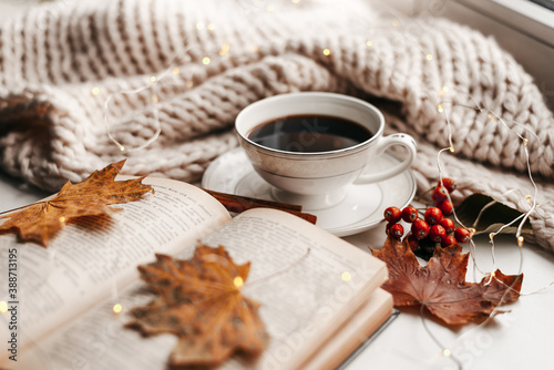 Autumn morning coffee. Cup of coffee and book on a plaid against the background of autumn leaves. Still life concept.