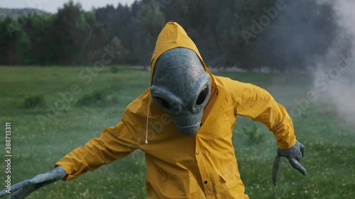 aliens dance in smoke. alien has arrived on earth and is standing in forest. an actor in alien costume, in yellow raincoat and khaki pants, touches his hands.UFO futuristic concept
