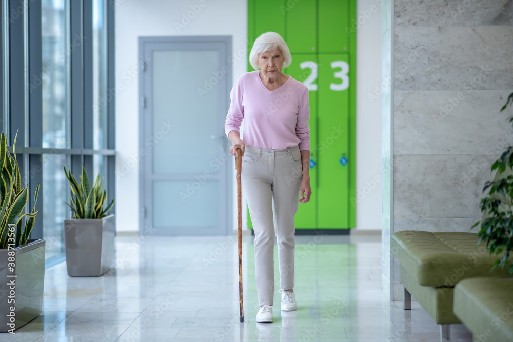 Elderly woman with a walking stick walking in the corridor Elderly woman with a walking stick walking in the corridor