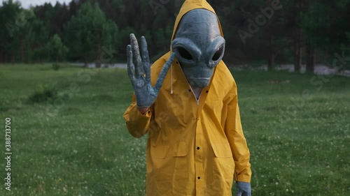 alien waved his hand and welcomed.alien has arrived on earth close up.an actor in alien costume, in yellow raincoat and khaki pants, touches his hands.UFO futuristic concept