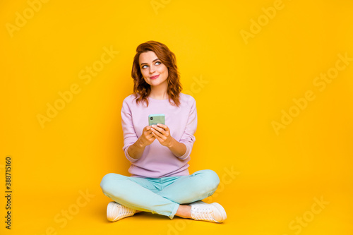 Full length photo of positive cheerful girl sit floor legs crossed folded use smartphone think thoughts comment post blog wear turquoise pink trousers isolated over bright color background
