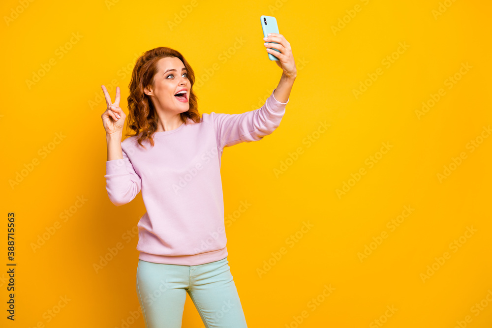Hello Photo of funny pretty lady hold telephone hand making selfies showing v-sign symbol saying hi wear pink sweater green pants isolated yellow color background