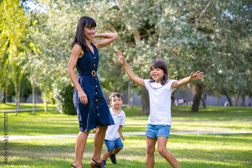 Two joyful kids and their mom playing active games on grass, having fun together in park. Family outdoor activity and leisure concept