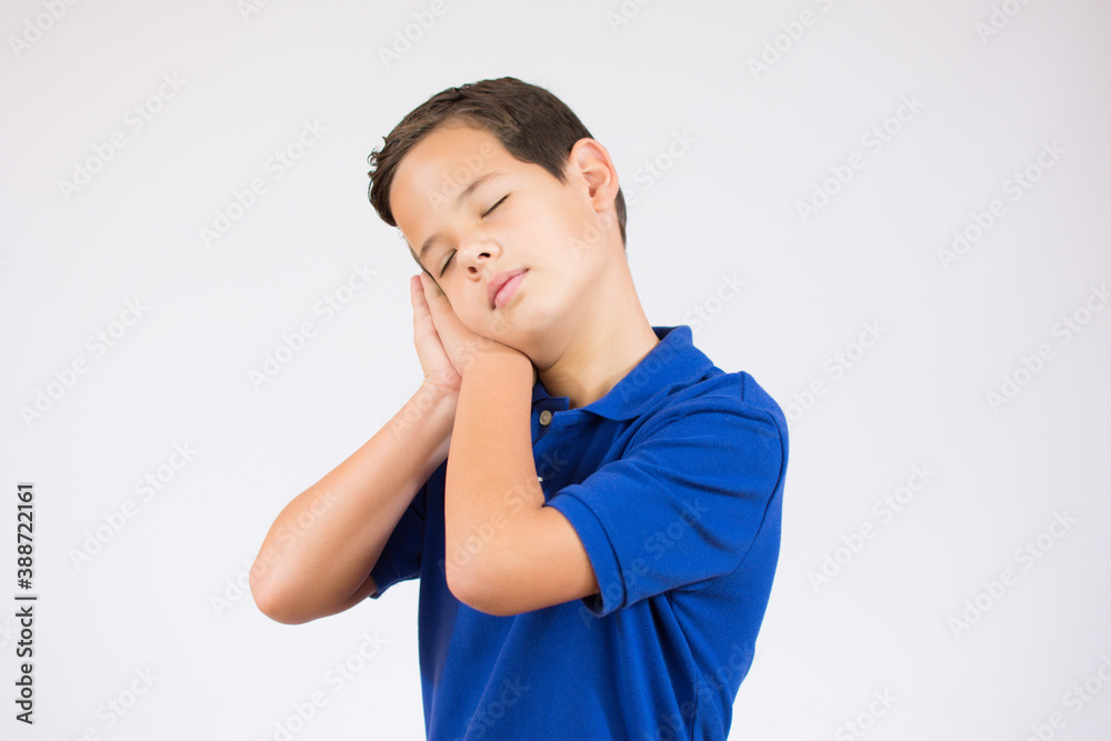 Relax and sleep time. Tired young handsome little boy with closed eyes leaning on palms as pillow pretending sleeping being exhausted seeing dreams standing against background. Sleeping gesture.