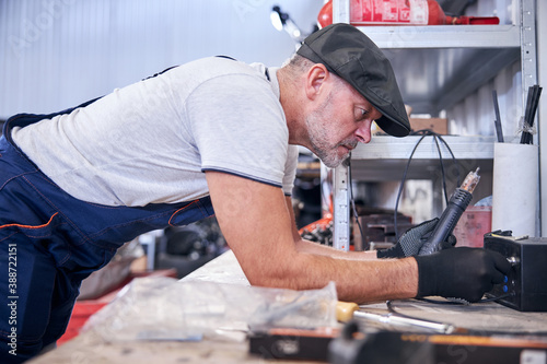 Bearded mechanic using electric device at car repair station