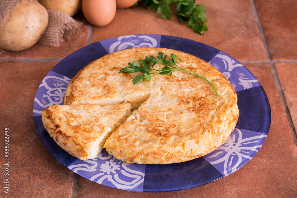 Spanish omelette made with potatoes, eggs and onion, with a piece of parsley on top, on a blue plate in a rustic kitchen 
