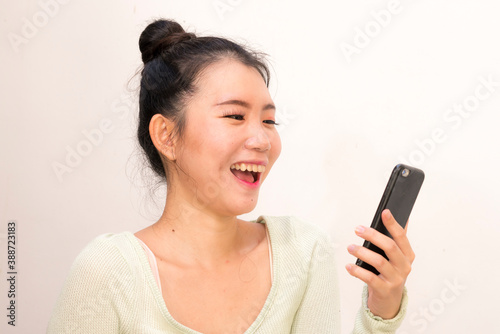 young attractive and sweet Asian Chinese woman laughing happy and cheerful using internet mobile phone isolated on studio background in communication concept