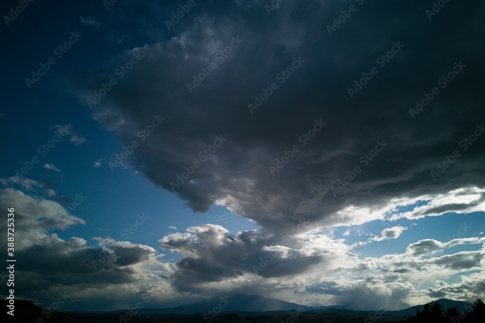 Enorme nuvola bianca e nera che si protende nel cielo azzurro da sopra le montagne Enorme nuvola bianca e nera che si protende nel cielo azzurro da sopra le montagne