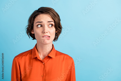 Closeup photo of sad depressed displeased lady horrified facial expression made huge big mistake feel guilty look side empty space bite lips wear orange shirt isolated blue color background photo