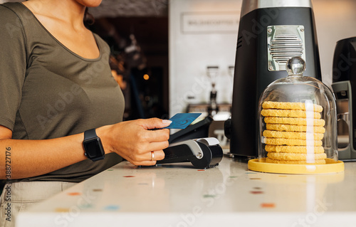 Side view of an unrecognizable woman paying with NFC technology on credit card in cafe