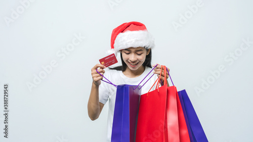 Beautiful attractive Asian woman with santa hat holding shopping bag and credit card in studio shot.
