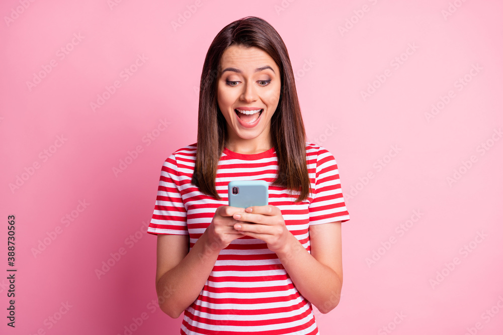 Portrait of excited girl looking phone smiling wear read white t-shirt isolated over pastel pink background Portrait of excited girl looking phone smiling wear read white t-shirt isolated over pastel pink background