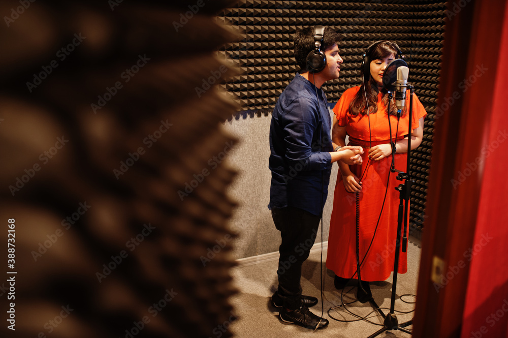 Young asian duet singers with microphone recording song in record music studio.