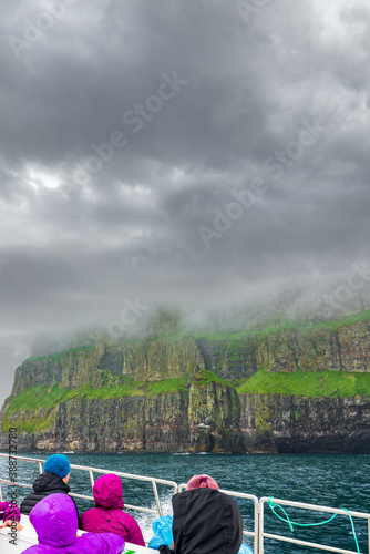 Unrecognizable tourists over boat observing impressive Vestmanna cliffs