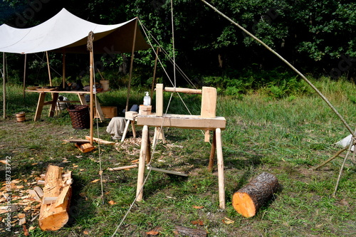 A close up on a wood chopping station with two logs on both sides of it seen next to a cloth tent on wooden beams seen in the middle of a field or meadow on a sunny summer day in Poland 