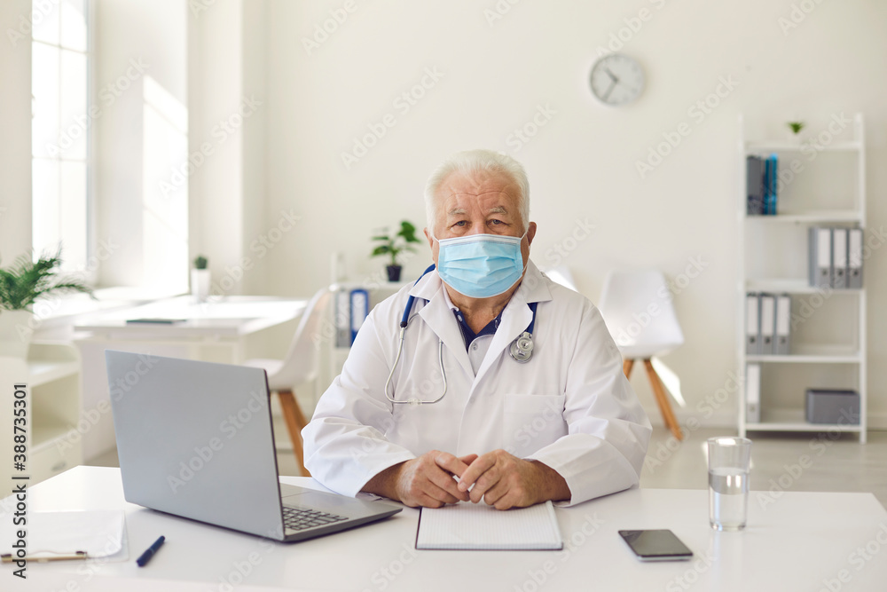 Senior experienced doctor in uniform sitting near laptop during videocall and online meeting