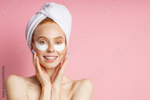 Headshot of sensual beautiful woman applying patches to reduce under eye puffiness and dark circles, touching gently face with both palms, posing naked isolated on pink background. Beauty concept.