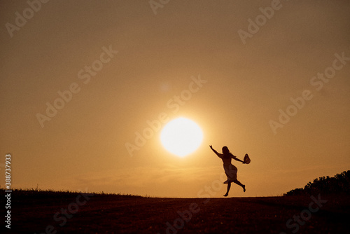 Fototapeta Naklejka Na Ścianę i Meble -  Silhouette of a woman running towards the sun with outstretched hand.
