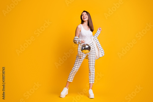 Full size photo of positive nice brown hair girl hold disco ball dance wear suit shoes isolated over yellow background