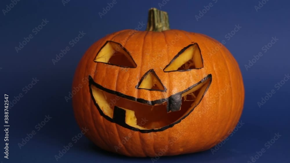 Jack-o-lantern for a Halloween party stands on a table against a dark background. Halloween pumpkin or jack-o-lantern with glowing eyes on a blue background. Jack-o-lantern for a Halloween party stands on a table against a dark background. Halloween pumpkin or jack-o-lantern with glowing eyes on a blue background.