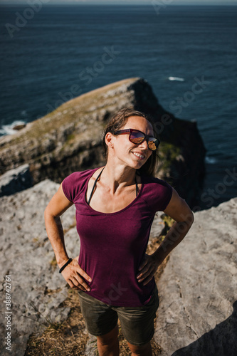 Happy natural woman portrait, with sunglasses, enjoying outdoors in the coast, with a rock in the background. © daviles