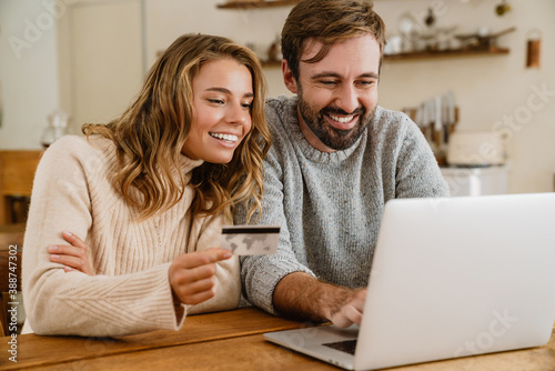 Happy couple using laptop and credit card while sitting in kitchen