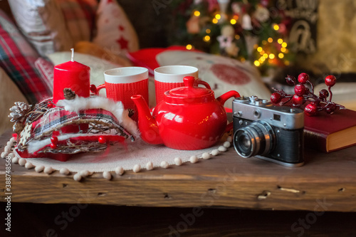 New Year's red tea set on the table next to the bed. There are pillows on the bed. Christmas lights are on. A camera and a book on the table