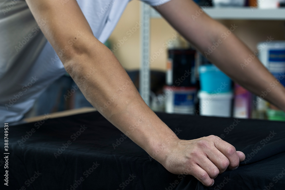 close-up of a person's hands spreading a dark T-shirt on the print screening apparatus. selective focus photo. serigraphy production. printing images on t-shirts in a design studio.