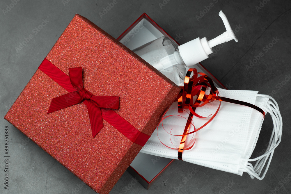 Present, gift box open with hand sanitizing gel and protective masks inside. Dark stone gray background. Holidays, and partys during coronavirus social distance concept.