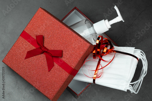 Present, gift box open with hand sanitizing gel and protective masks inside. Dark stone gray background. Holidays, and partys during coronavirus social distance concept.