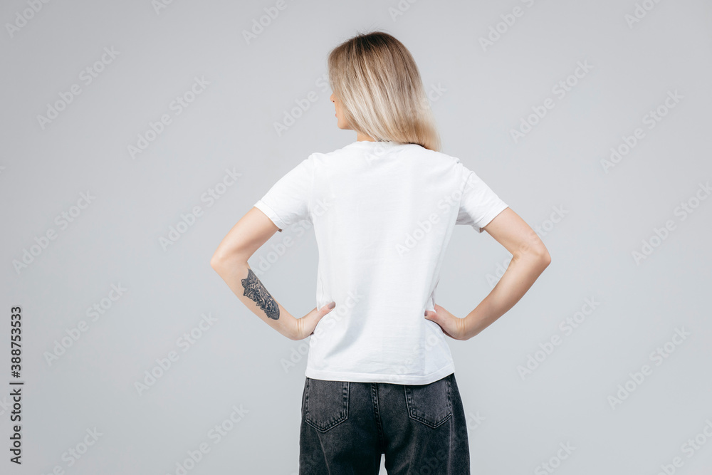 Back of stylish blonde girl wearing white t-shirt posing in studio - obrazy, fototapety, plakaty 