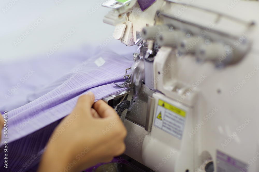 The worker is sewing a textile with a sewing machine in a fabric factory. The worker is sewing a textile with a sewing machine in a fabric factory.