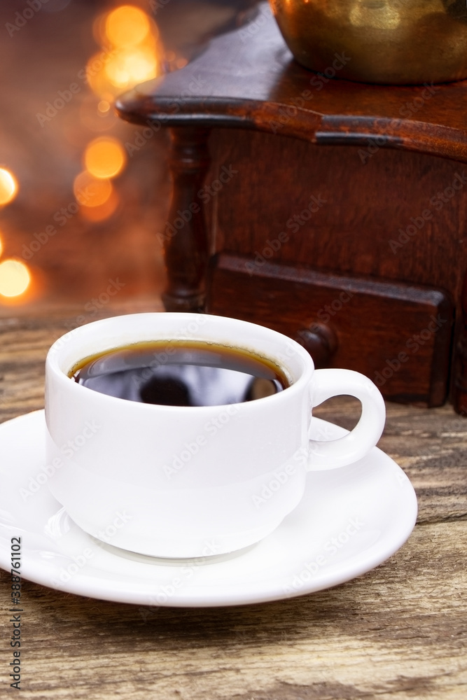 A white cup of coffee on a wooden background. A coffee grinder on a wooden table. Cup of espresso