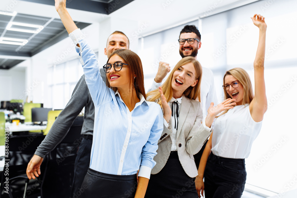 Naklejka premium Successful excited business team standing together celebrating victory showing victory gesture while working in office