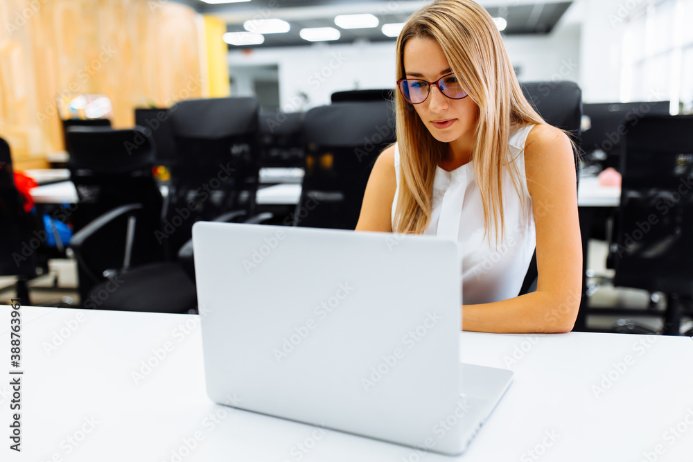 Successful attractive business woman using laptop while sitting at work table in office Successful attractive business woman using laptop while sitting at work table in office