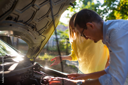 The woman and the man are repairing the car. The couple looks under the hood of the car. Auto mechanic and female customer. A man mechanic and woman customer look at the car hood and discuss repairs.