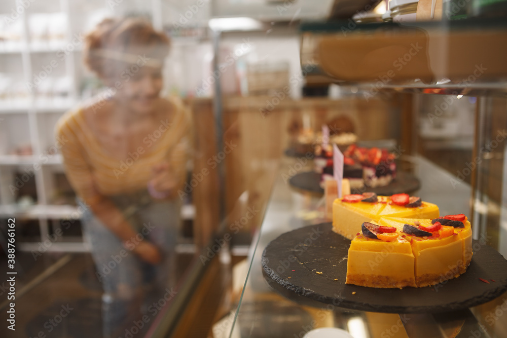 Selective focus on delicious raw vegan cake on the display, female customer on background, copy space