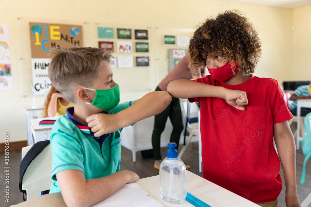 Two boys wearing face masks greeting each other by touching elbows at school Two boys wearing face masks greeting each other by touching elbows at school