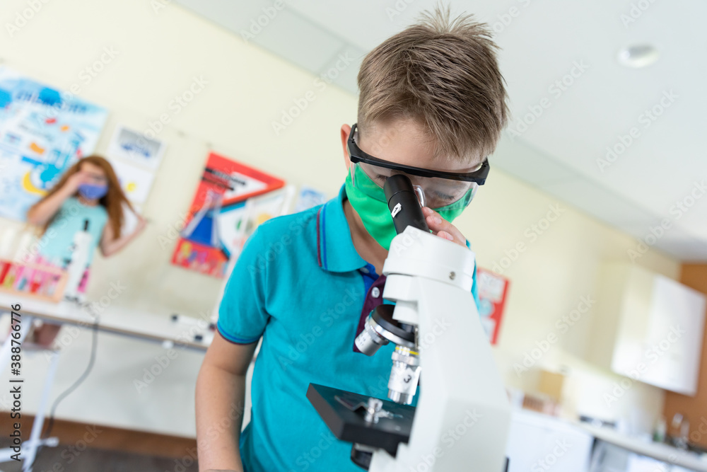 Boy wearing face mask and protective glasses using microscope in laboratory Boy wearing face mask and protective glasses using microscope in laboratory