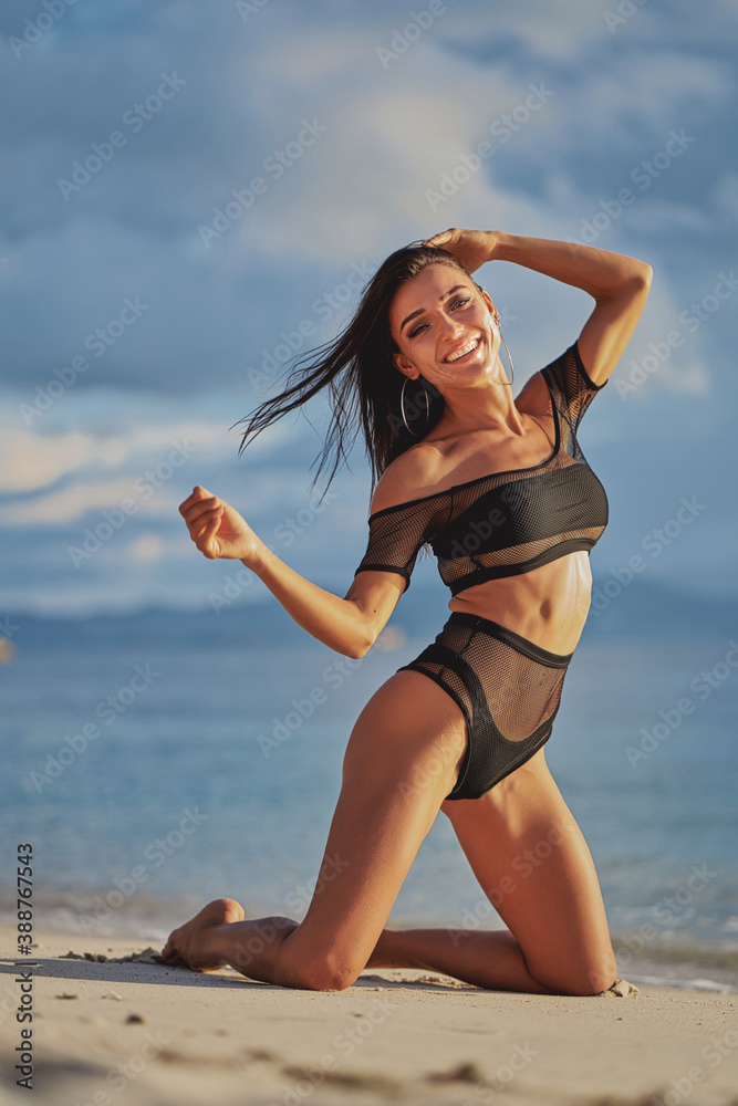 Woman at the sea. Beautiful young woman standing on her knees on a sandy beach