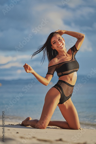 Obraz na płótnie Woman at the sea. Beautiful young woman standing on her knees on a sandy beach w salonie