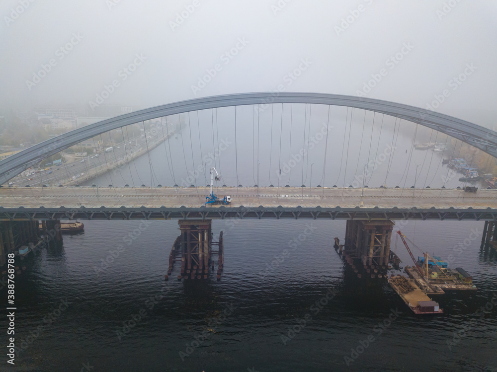 Fototapeta premium Aerial drone view. Construction of a cable-stayed bridge across the river in dense fog.