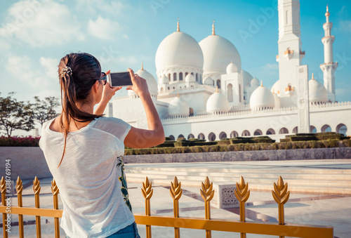 Young tourist woman shooting on mobile phone Sheikh Zayed great white mosque in Abu Dhabi, United Arab Emirates, Persian gulf. UAE is famous tourism destination